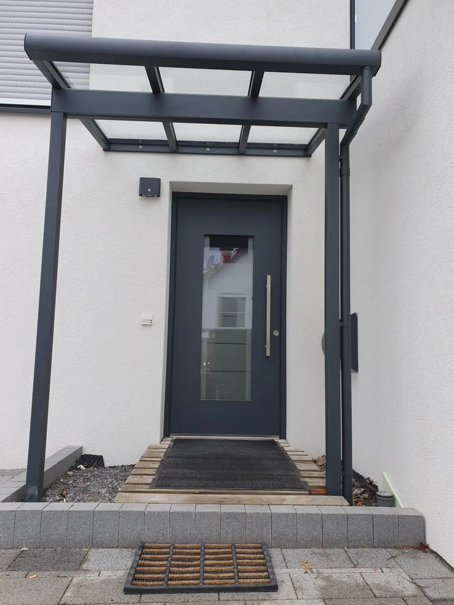 Anthrazitfarbene Aluminium-Haustür mit schmalem Lichtband unter einem Glasvordach
